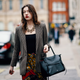 LONDON, ENGLAND - FEBRUARY 16: A guest wears a houndstooth jacket, a large necklace, a black top, a black Celine backpack, colorful floral print pants, during London Fashion Week February 2019 on February 16, 2019 in London, England. (Photo by Edward Berthelot/Getty Images)